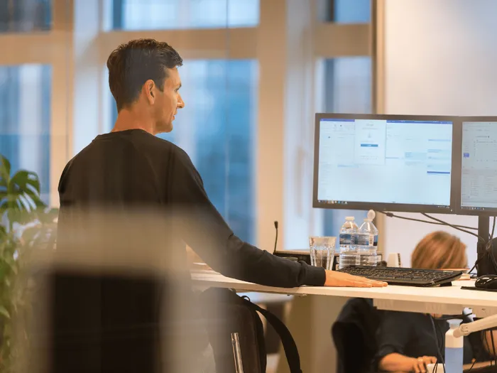 RS-blog-omzetrapportages-voor-legalsense Een medewerker van RS Finance staat voor twee computer monitors