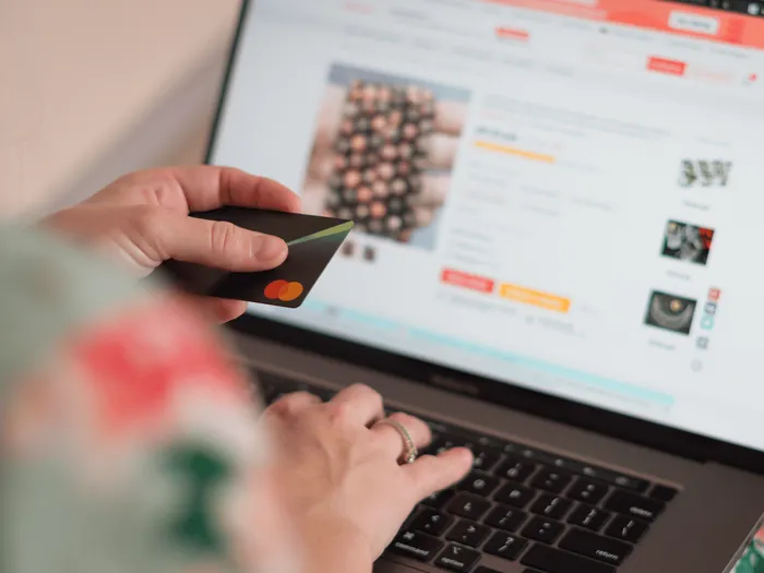 RS-blog-payment-service-providers Een persoon die een creditcard vasthoudt terwijl hij/zij een webshop bezoekt op zijn/haar laptop.