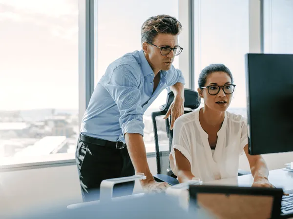 Twee personen die op een computer werken in een kantoor.