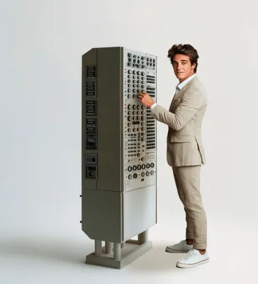 Een persoon in een pak staat naast een machine met heel veel knopjes.