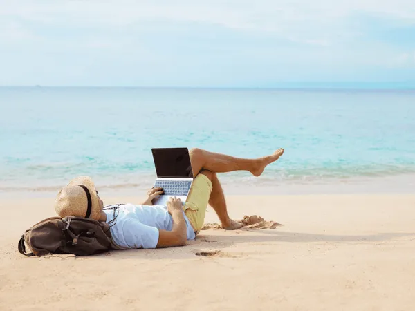 Een persoon met een laptop op het strand.
