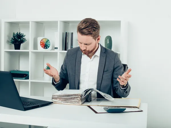 Een persoon die aan een bureau zit met een laptop en papieren