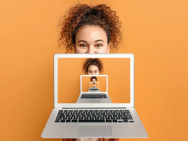 Een persoon met krullend haar die een laptopscherm omhoog houdt