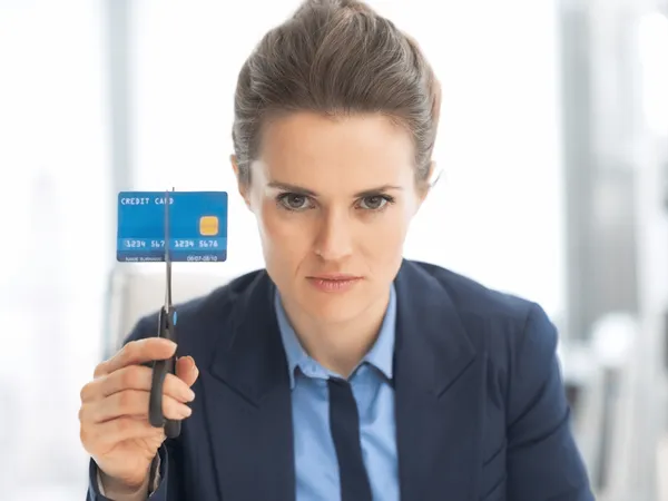 Een persoon in een pak die een creditcard tussen een schaar omhoog houdt