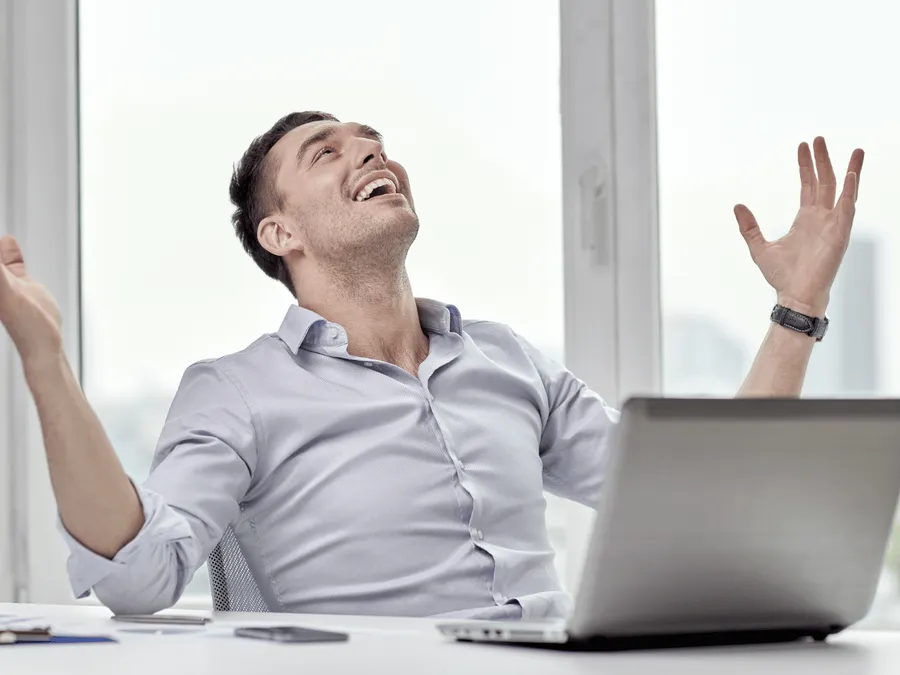 Een persoon die glimlacht terwijl hij aan een bureau zit met zijn handen in de lucht