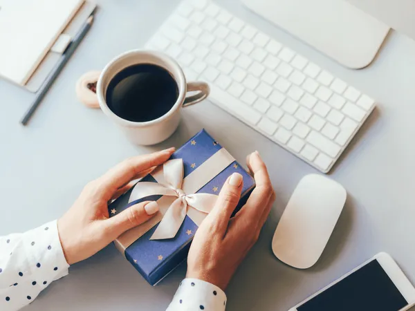 RS-blog-WKR Handen met blauw kerstcadeau op bureau met koffie en toetsenbord – bedrijfskerstgeschenken en werkkostenregeling