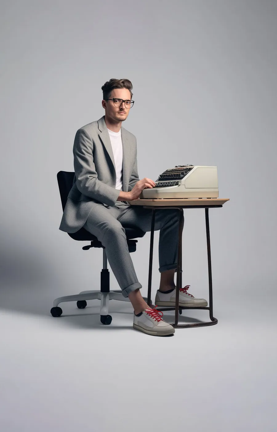 RS-Finance-fiscale-aangiften-en-advies Man met bril in pak met sneakers zit aan een kleine tafel met oude typewriter.