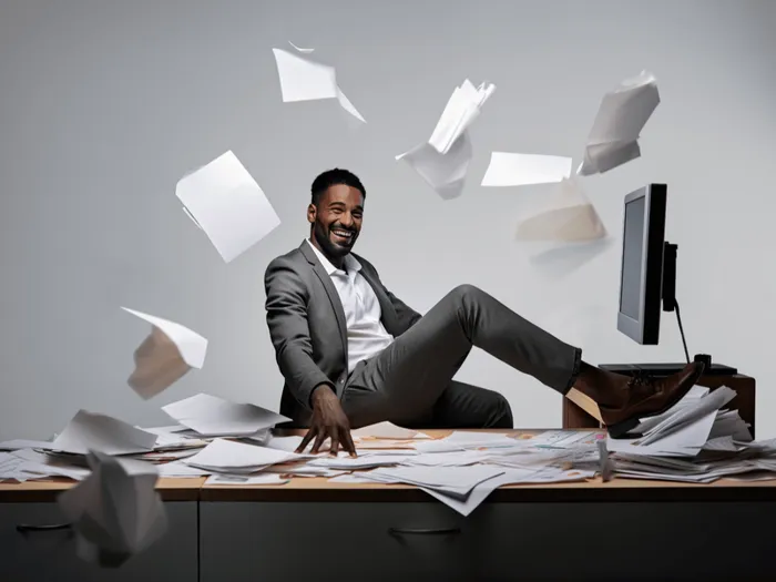 Man met zijn voet op een bureau met vliegende paperassen om zich heen